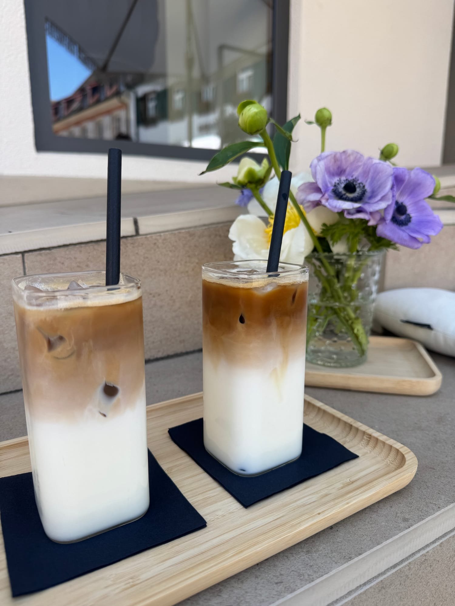 Zwei geschichtete Eis-Lattes auf einem Bambustablett mit Anemonen