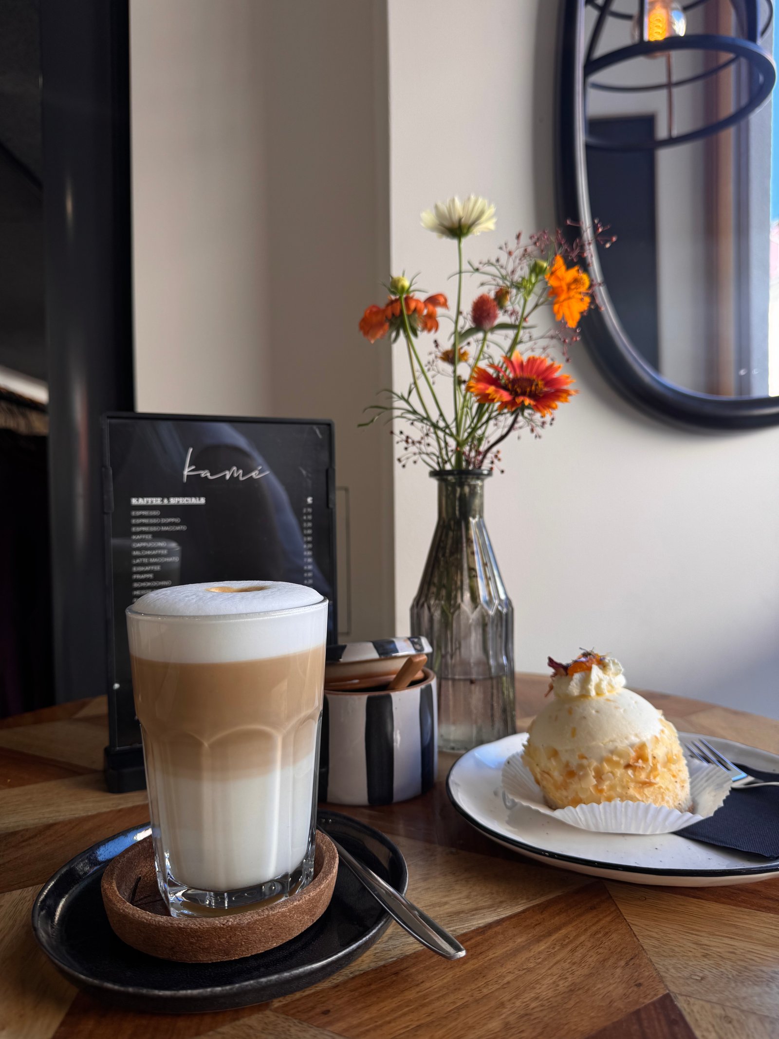 Latte, Blumen und kleines Dessert auf einem Café-Tisch