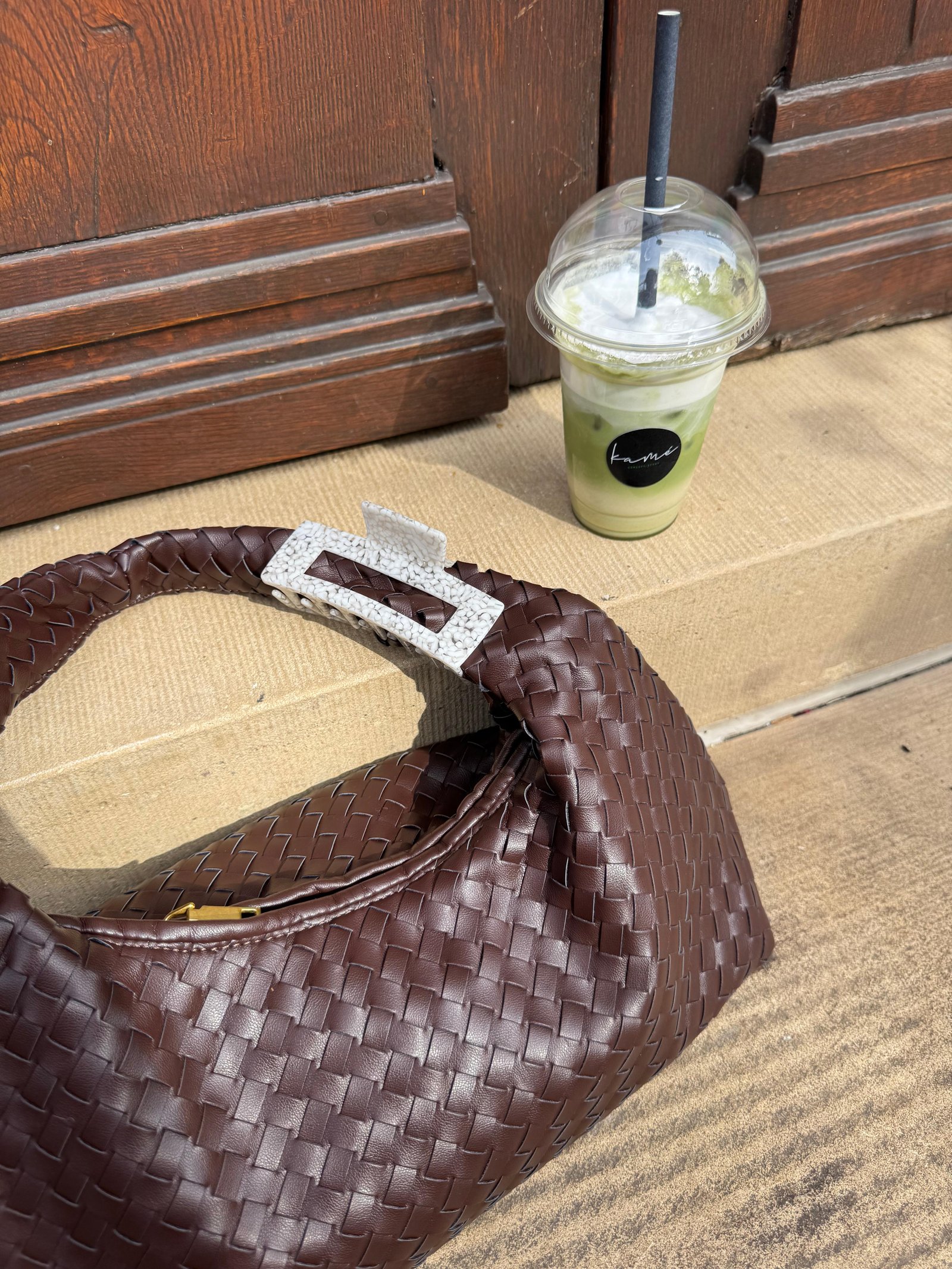 Geflochtene braune Tasche mit Matcha-Drink vor einer Holztür