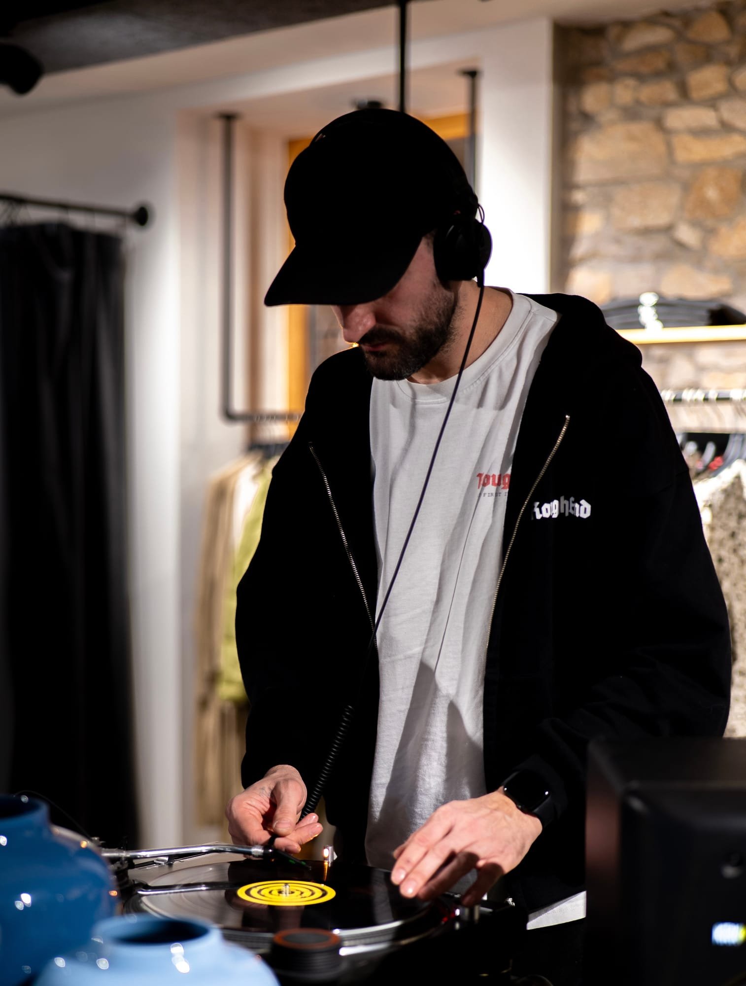 DJ mit Kopfhörern an den Plattentellern neben Kleiderstangen