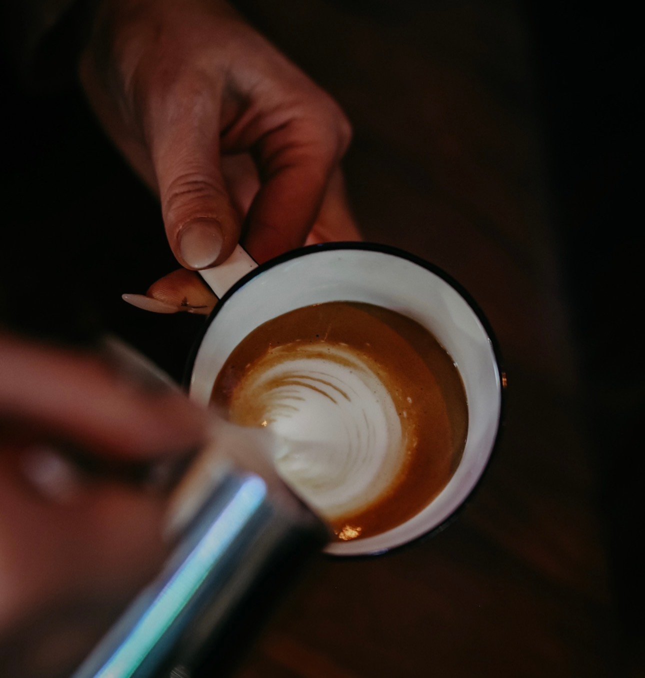 Barista-Hand beim Eingießen von Milch in einen Espresso